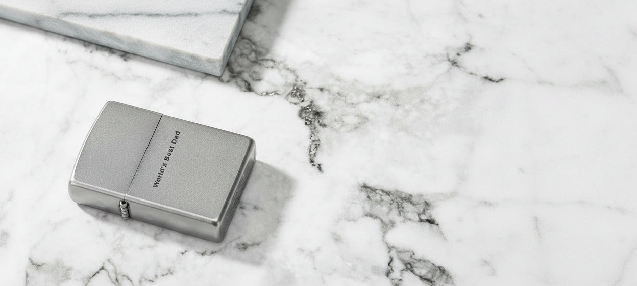 A silver metal lighter with engraved text reading 'WATERLOO SIDE STAND' resting on a white and gray marble surface.